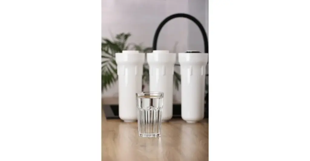 Copo de água cristalina com refil e filtro de purificador ao fundo, representando água pura e filtragem eficiente.