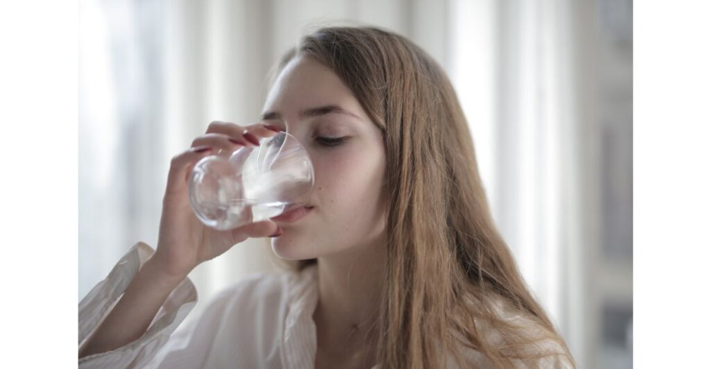 Mulher jovem bebendo água purificada em um copo transparente, transmitindo a ideia de água limpa e segura para consumo.