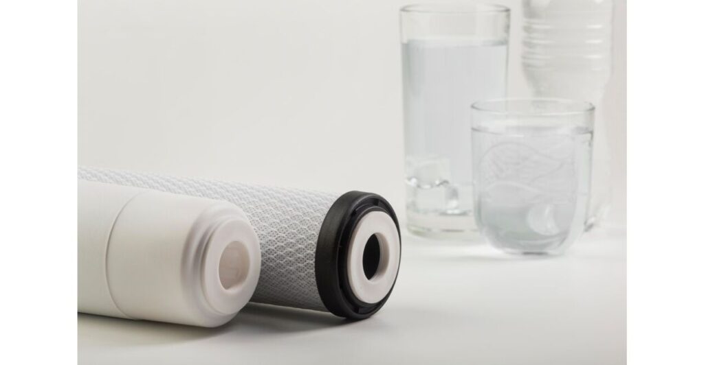 Duas velas de filtro de água ao lado de um copo com água limpa, sobre fundo branco.