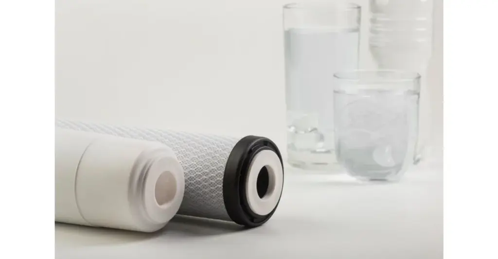 Duas velas de filtro de água ao lado de um copo com água limpa, sobre fundo branco.