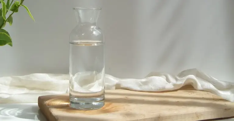 Jarra de água transparente com filtro de carvão ativado em cima de uma mesa de madeira, ilustrando purificação caseira de água.