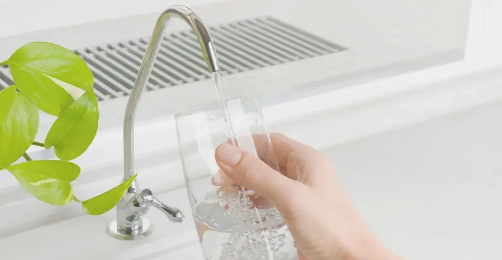 Mão enchendo um copo de água em uma torneira com filtro Lorenzetti Acqua Bella, garantindo água limpa e purificada. Imagem do Canva