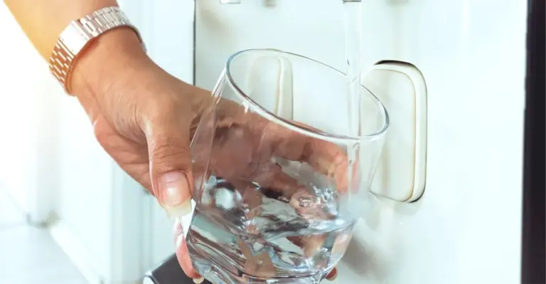 Copo sendo enchido com água filtrada diretamente de um purificador de água na cozinha.