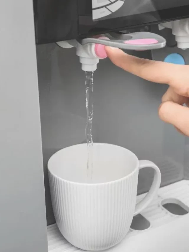 mão de uma pessoa enchendo um copo de água em um filtro de água